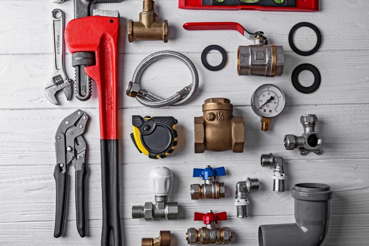 A collection of plumbing tools and accessories arranged neatly on a white table, showcasing wrenches, pipes, and fittings.